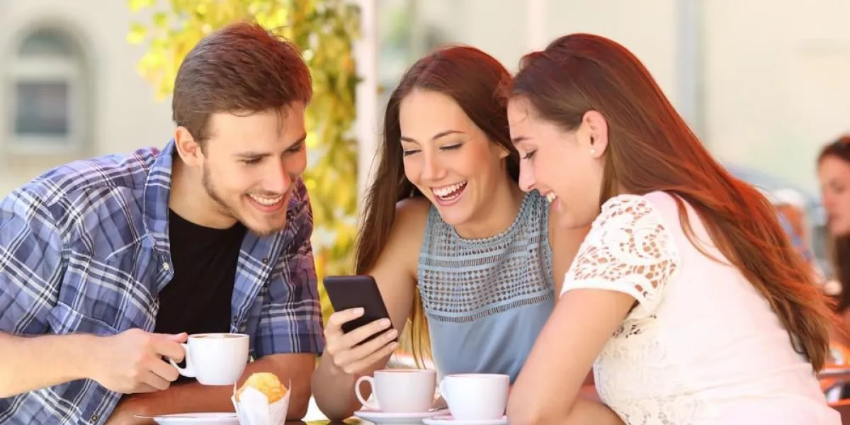 trois amis heureux, regarder les médias sociaux dans un téléphone intelligent dans un café