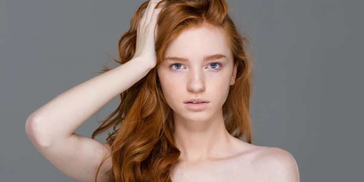 portrait de beauté de tendre jolie jeune femme avec de beaux longs cheveux roux sur fond gris