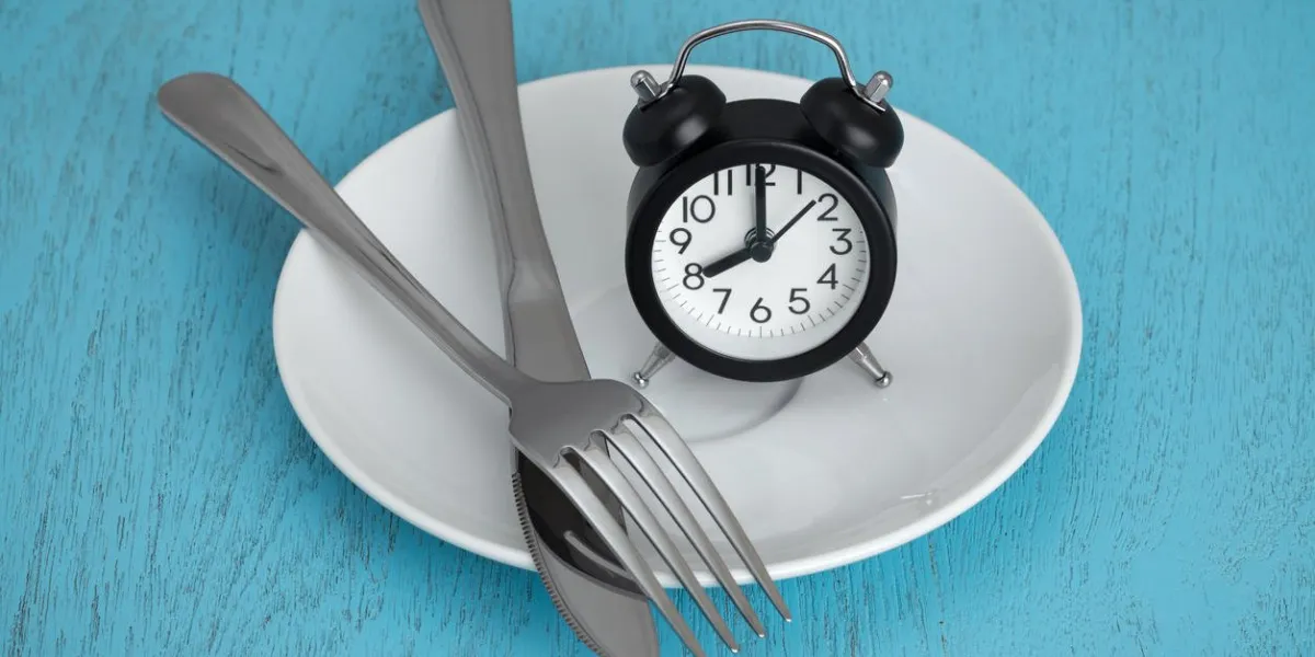 intermittent fasting concept with clock on white plate, fork and knife on blue table
