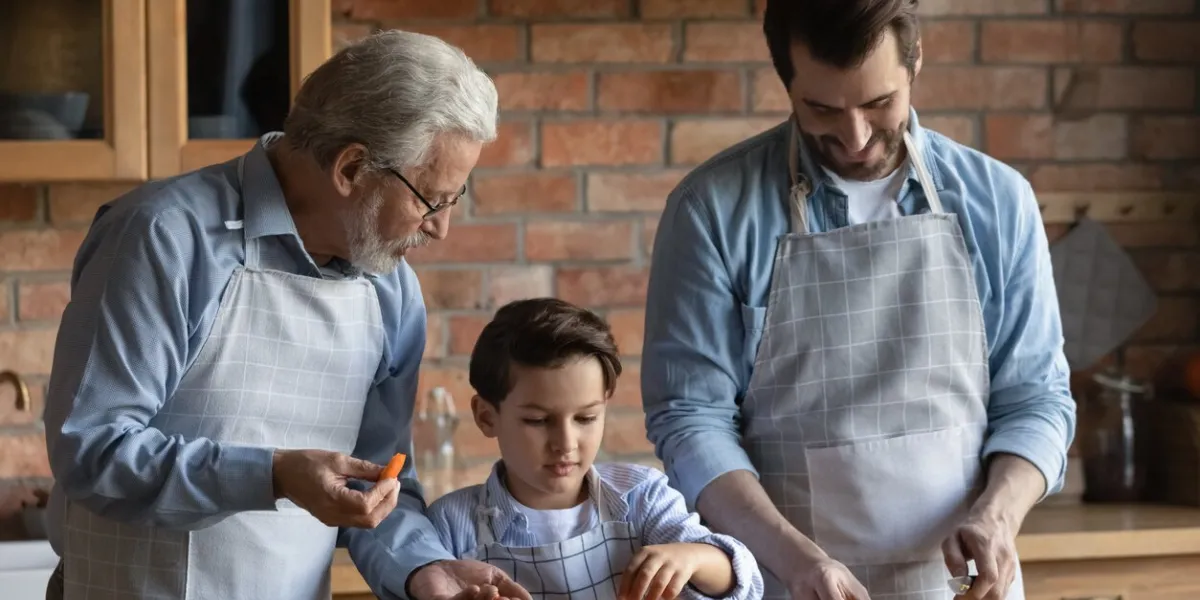 happy three generations of caucasian men have fun cooking healthy dinner or lunch at home together smiling little boy child with father and grandfather prepare food salad in kitchen diet concept