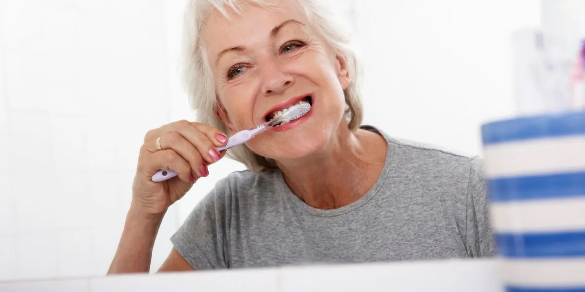 senior woman in bathroom brushing teeth at home