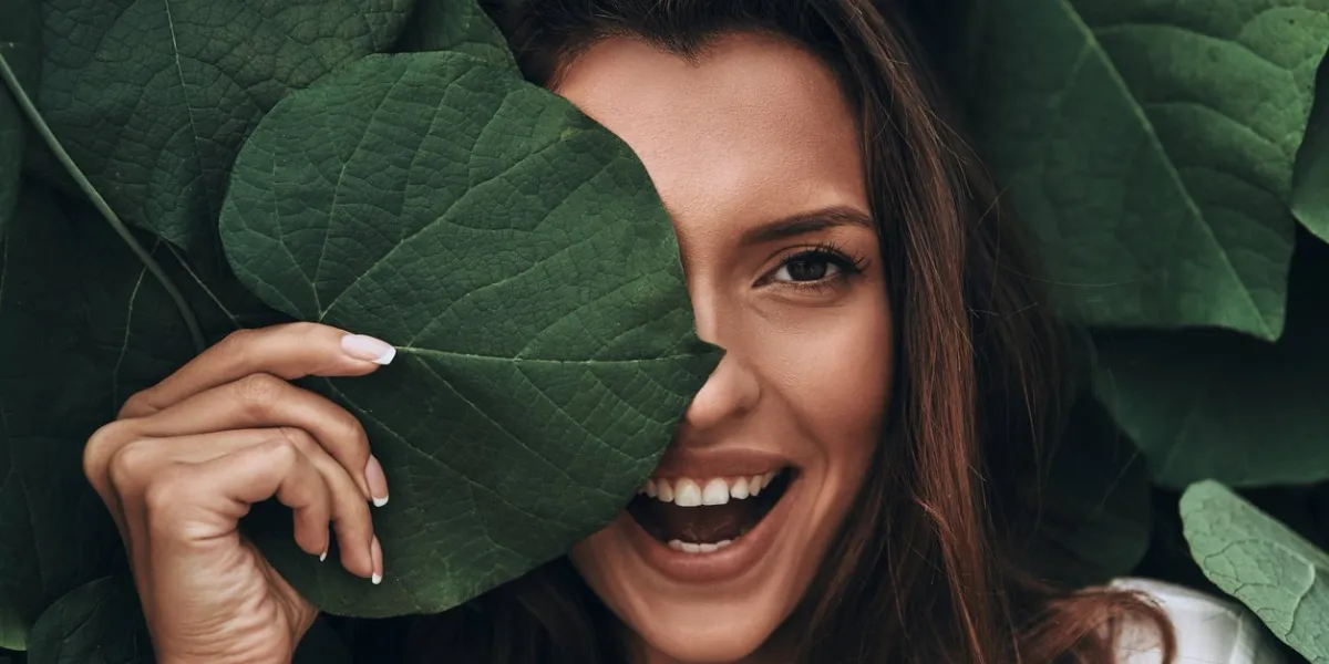 attractive young woman looking at camera and smiling while standing among the leaves outdoors