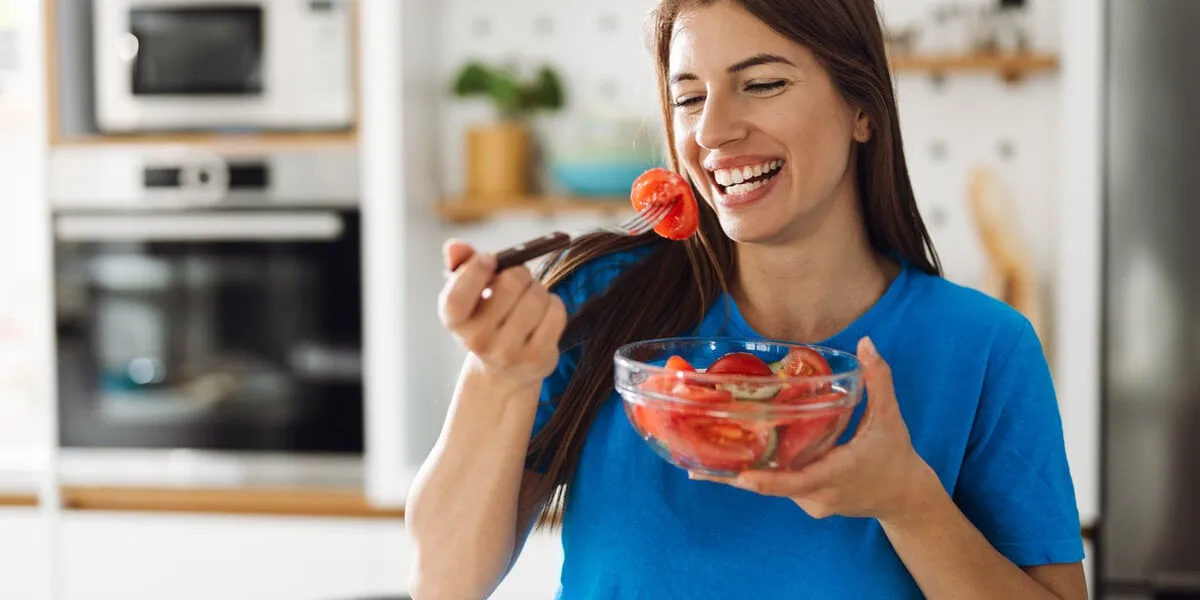 smiling woman eating salad in the kitchen