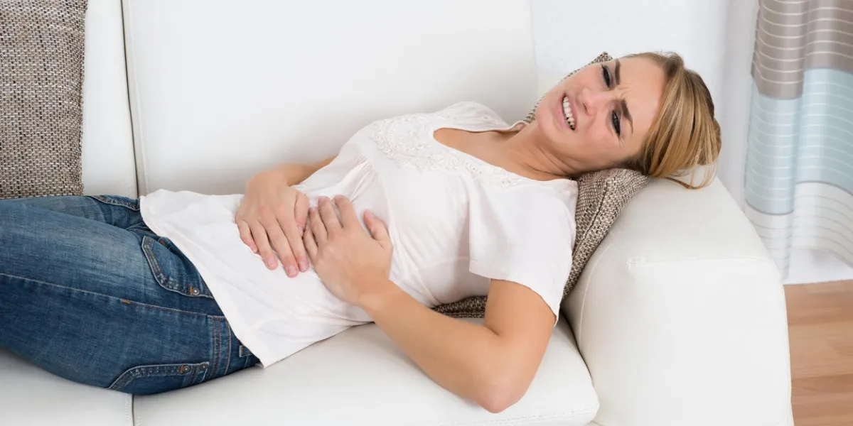 young woman suffering from stomach pain while lying on sofa at home