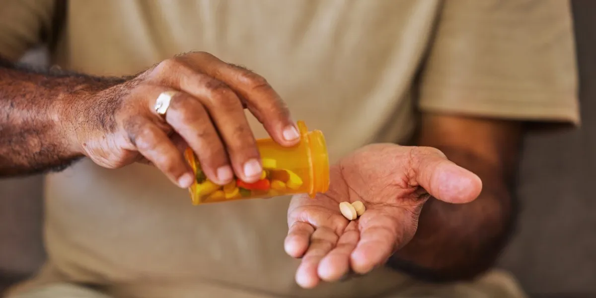 medicine, healthcare and pills in the hands of a senior man sitting on a sofa in the retirement home prescription, medication and antibiotics for chronic treatment and wellness with a pensioner