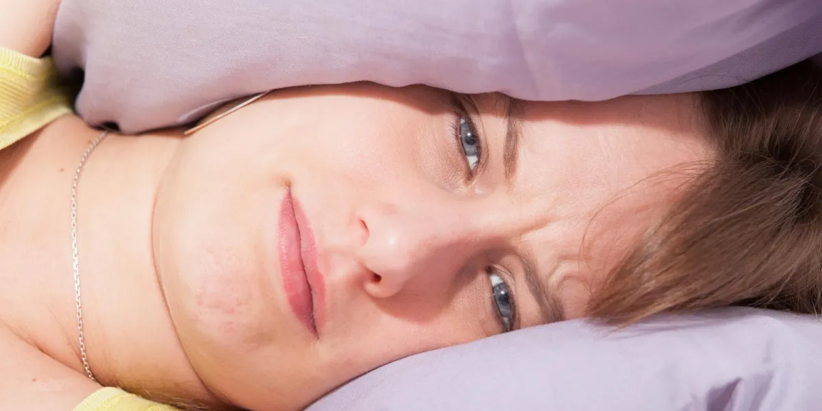femme avec sa tête sous son oreiller, essayant de dormir