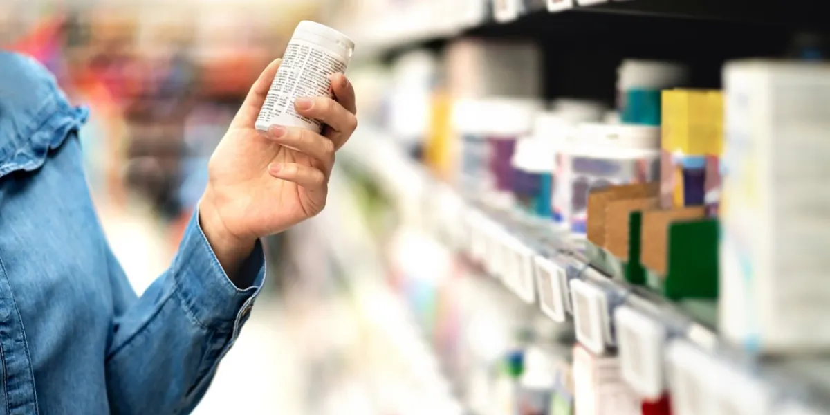 customer in pharmacy holding medicine bottle woman reading the label text about medical information or side effects in drug store patient shopping pills for migraine or flu vitamin or zinc tablets