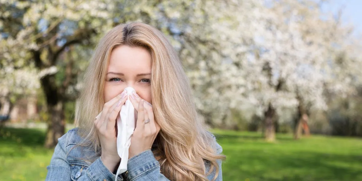 femme avec allergie éternuer dans un mouchoir avec des arbres en fleurs en arrière-plan