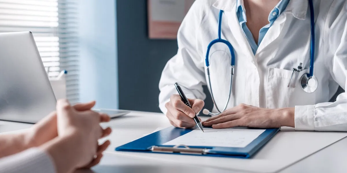 doctor sitting at desk and writing a prescription for her patient