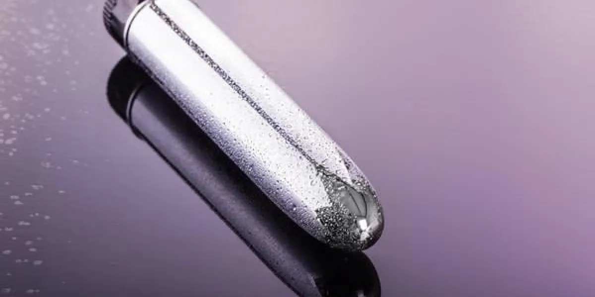 un vibrateur dildo métallique brillant et humide sur une surface réfléchissante sombre