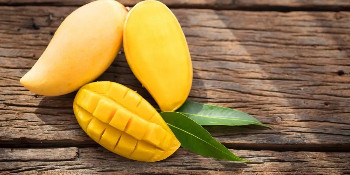 sliced ripe mango on wooded board with green leaves top-view