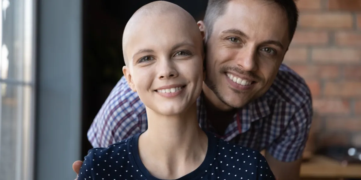 portrait of happy young man hugging beloved woman with cancer, looking at camera, smiling loving husband embracing hairless wife, giving support, motivation to win from oncology illness head shot