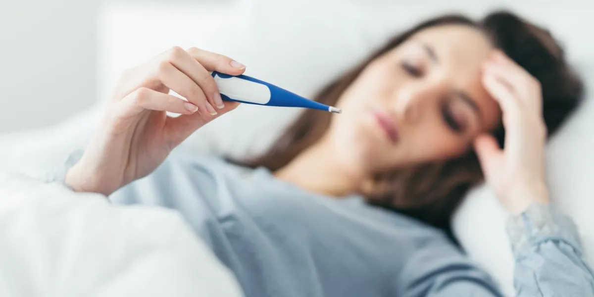 femme avec le virus de la grippe couchée dans son lit, elle mesure sa température avec un thermomètre et touche son front