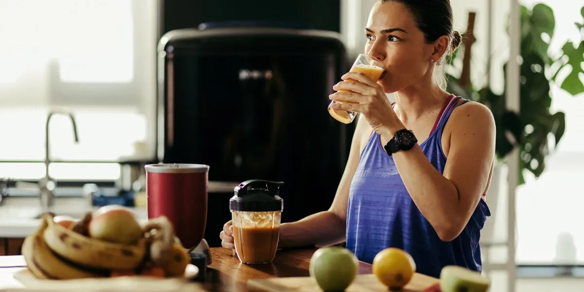yong sportswoman drinking fruit juice she made in a blender at home
