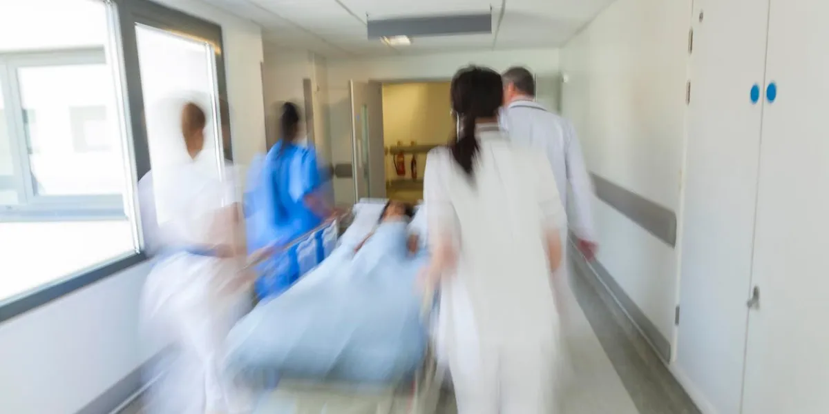 a motion blurred photograph of a child patient on stretcher or gurney being pushed at speed through a hospital corridor by doctors & nurses to an accident and emergency room