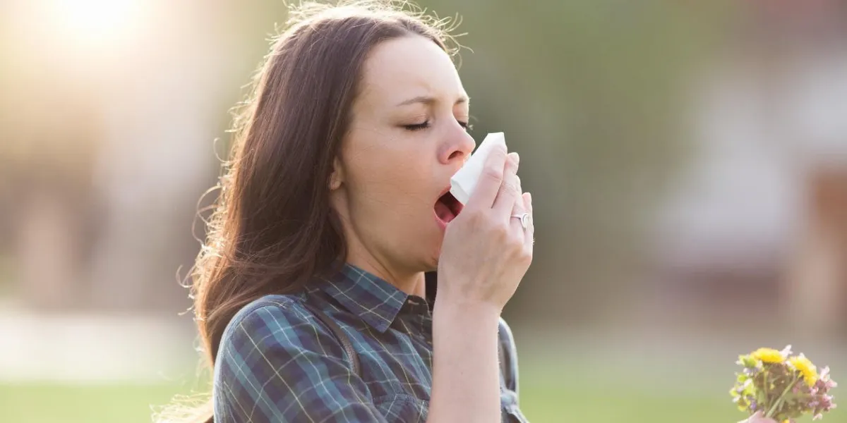 young pretty woman sneezing and blowing nose while holding bouquet of spring flowers from meadow pollen allergy symptoms
