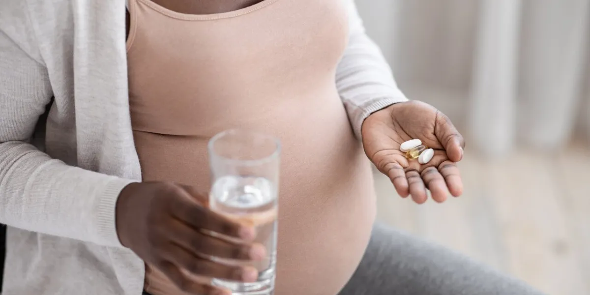 prenatal vitamins and supplements unrecognizable black pregnant woman taking pills capsules and glass of water, using medicaments for healthy pregnancy, cropped image, closeup