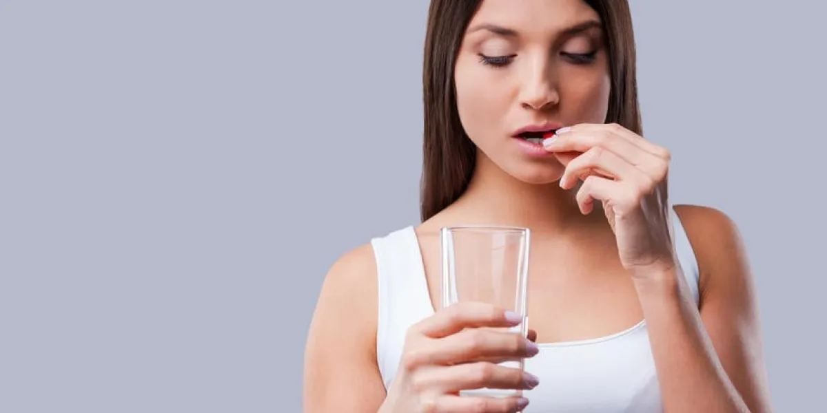 jeune femme déprimée prenant une pilule en se tenant debout sur fond gris