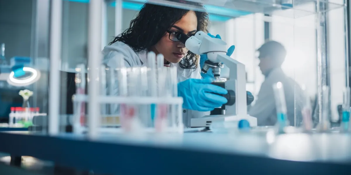 medical science laboratory  portrait of beautiful black scientist looking under microscope does analysis of test sample ambitious young biotechnology specialist, working with advanced equipment