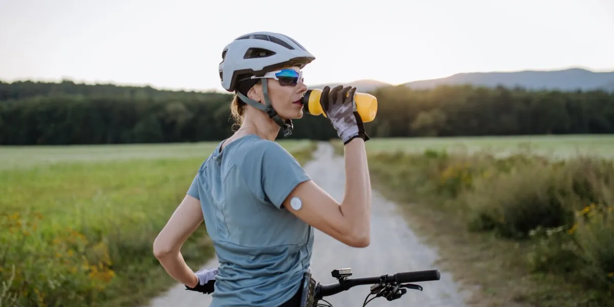 diabetic cyclist with a continuous glucose monitor on her arm drinking water during her bike tour to manage her diabetes while exercising concept of exercise and diabetes