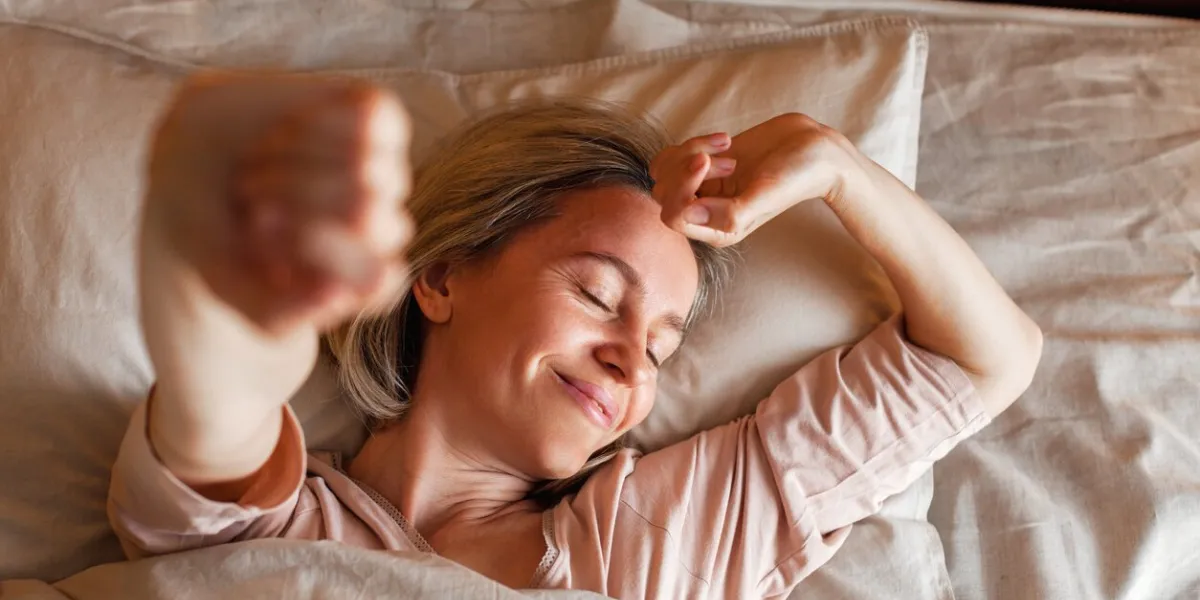 good morning, new day, weekend, holiday happy middle aged woman lying on bed, lady stretching arms after sleep and enjoying morning in cozy comfort bedroom interior, free space