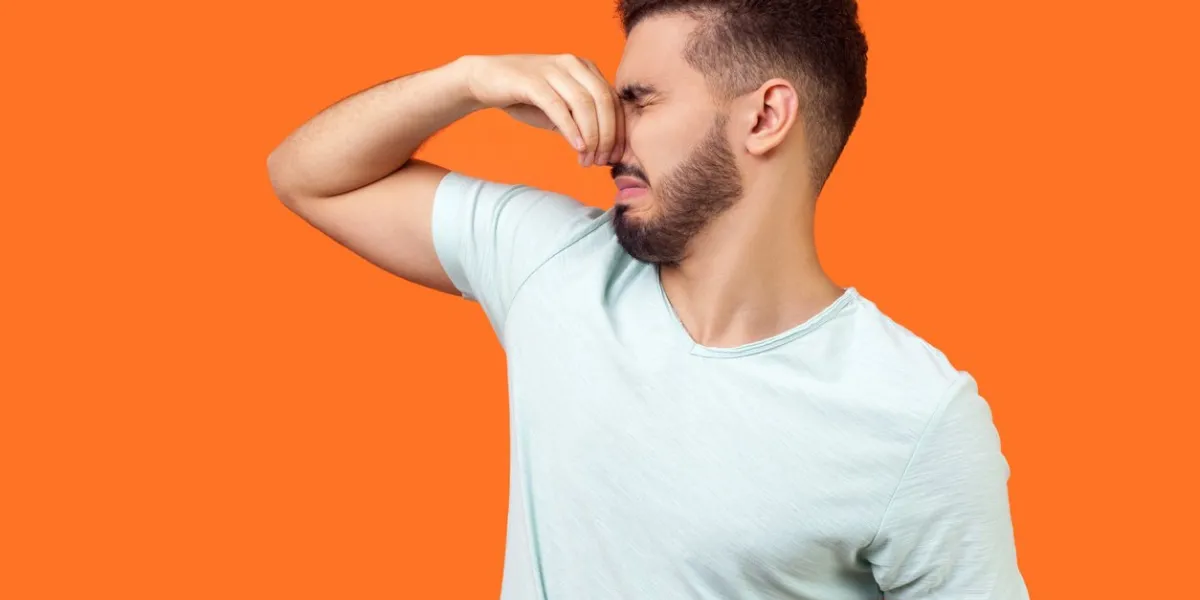 bad smell side view of confused unhappy brunette man with beard in white t-shirt holding breath with fingers on nose, turning away from stinky odor, fart studio shot isolated on orange background