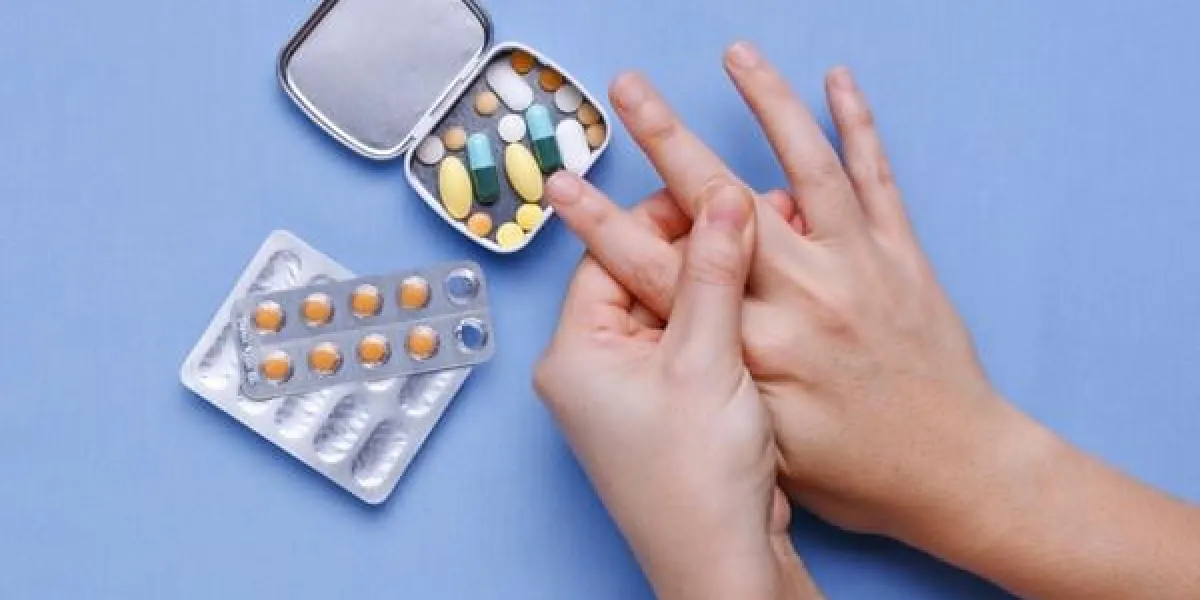 main de femme avec douleur au doigt et pilules sur la table