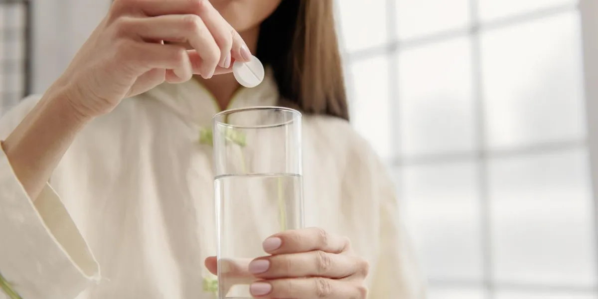 serious female putting pill in glass of water focus on medicament