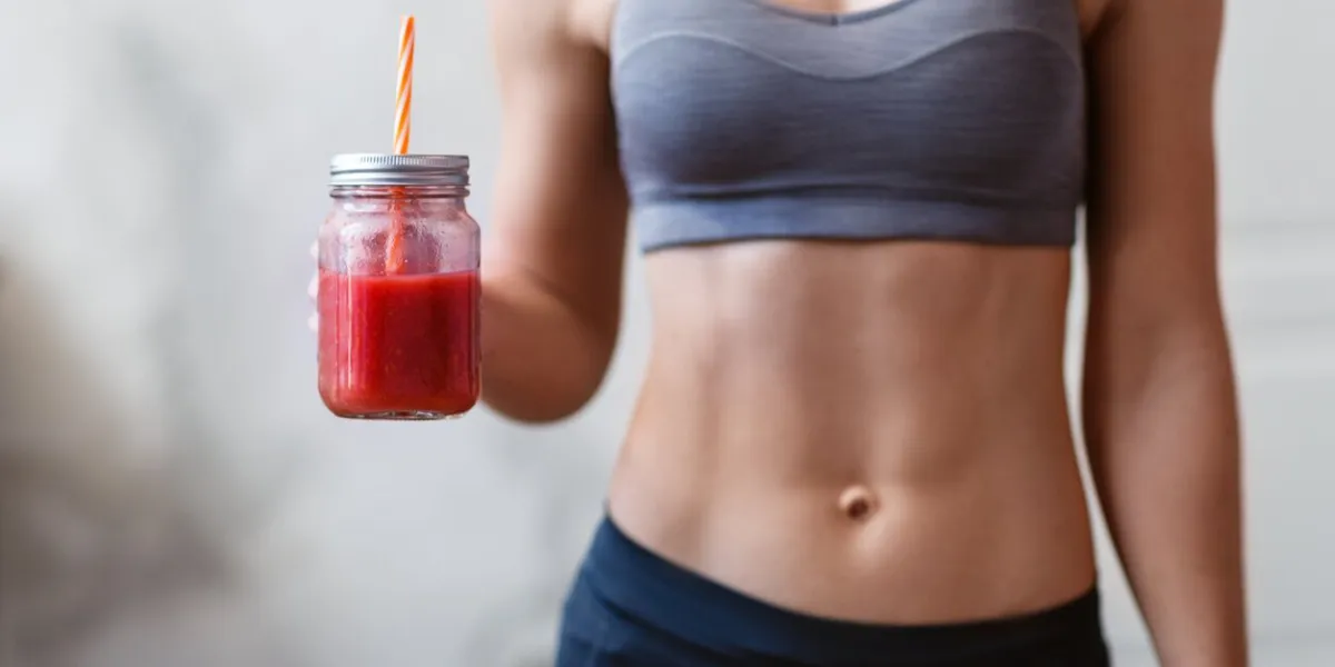 athletic woman holding friut red detox smoothie after fitness workout fitness and healthy lifestyle concept with beautiful sportive caucasian model in the room