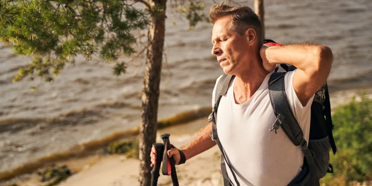 sporty man is feeling tired while going nordic walking with trecking sticks in nature near wavy pool