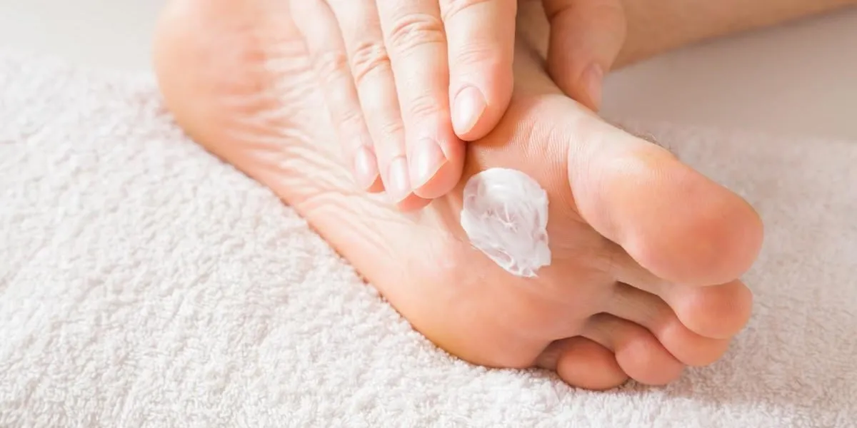 groomed, young man's hand applying feet moisturizing cream barefoot on the white towel cares about clean and soft legs skin healthcare concept
