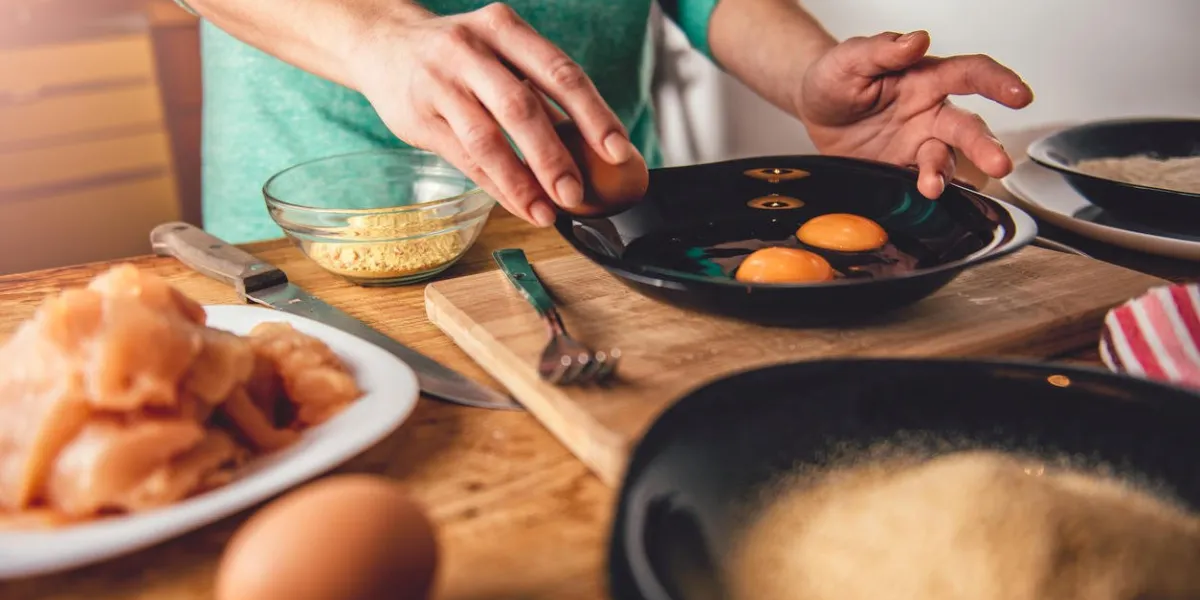 woman cooking and breaking eggs into the plate in the kitchen at home