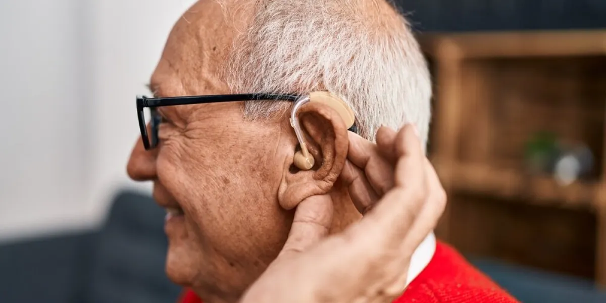 senior man smiling confident using deafness hearing aid at home