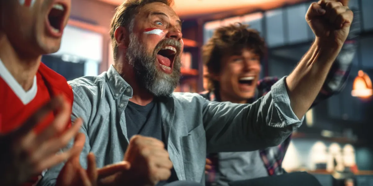 at home three joyfuls sports fans with painted faces sitting on a couch watch game on tv, celebrate victory when sports team wins championship friends cheer, shout portrait shot