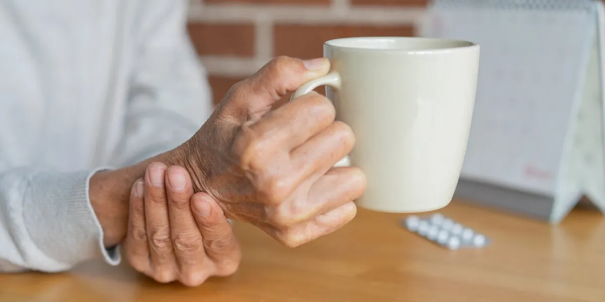 close up senior woman hand hold glass of waster for drink with unsteady at home for mature lifestyle and parkinson's symptom concept