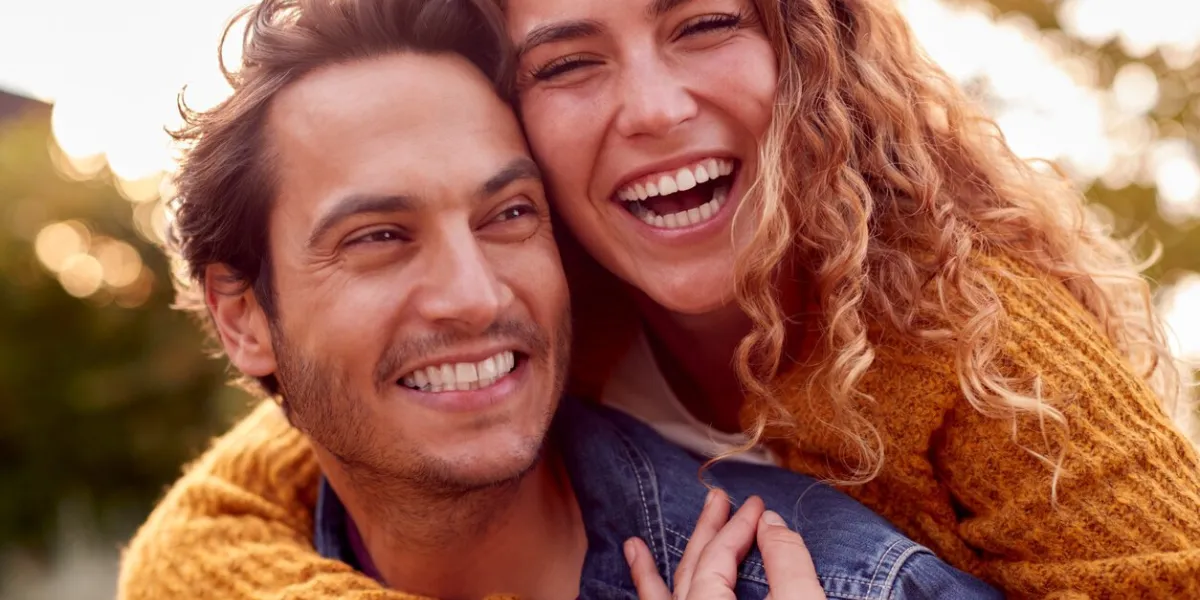 portrait of happy loving couple with man giving woman piggyback as they hug in autumn park together