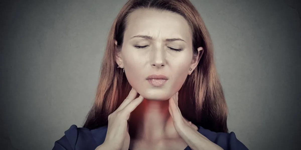 closeup girl with sore throat touching her neck colored in red sick young woman having pain in her throat isolated on gray wall background