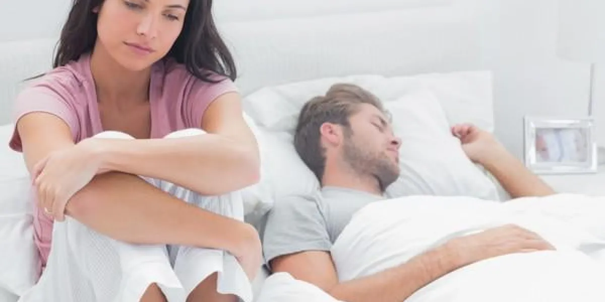 femme stressée dans son lit assis à côté de son partenaire de couchage