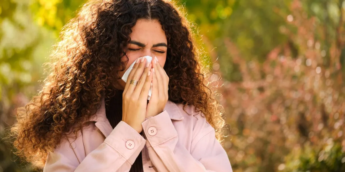 young caucasian woman with curly hair blowing your nose in a tissue at street in autumn