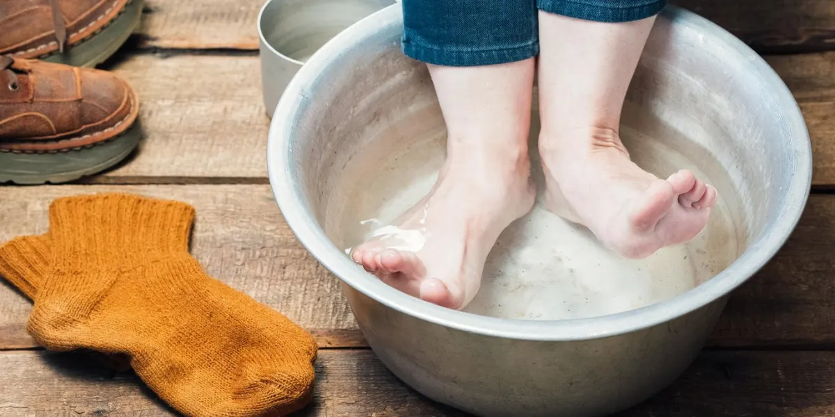 bain de pieds closeup pieds nus dans le bassin avec de l'eau chaude, des bottes et des chaussettes en laine sur le sol