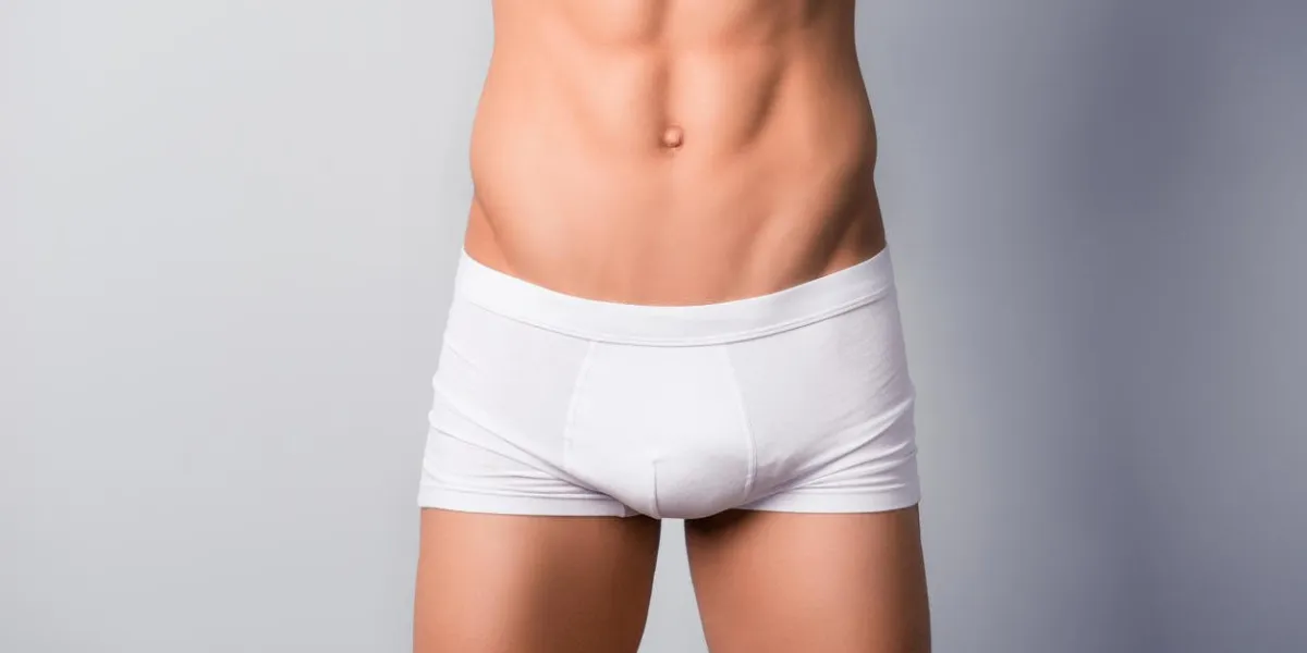 concept of man's health and vitility cropped close up photo of man's flat sporty abdomen, he is wearing white tight underwear, isolated on grey background