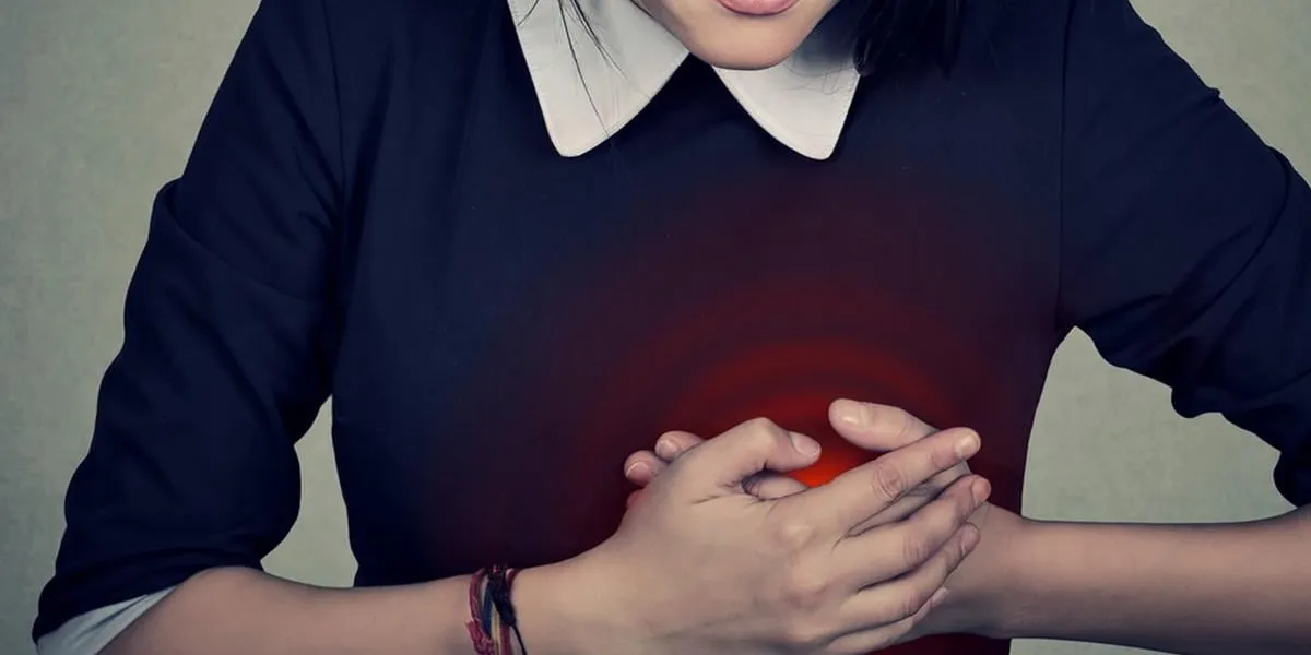 sick woman with heart attack, pain, health problem holding touching her chest colored in red with hands isolated on gray wall background human face expression