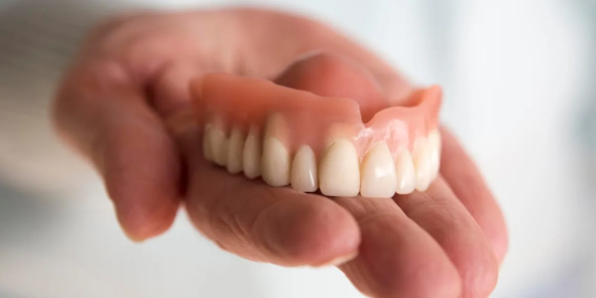 closeup of older womans hand holding a teeth denture