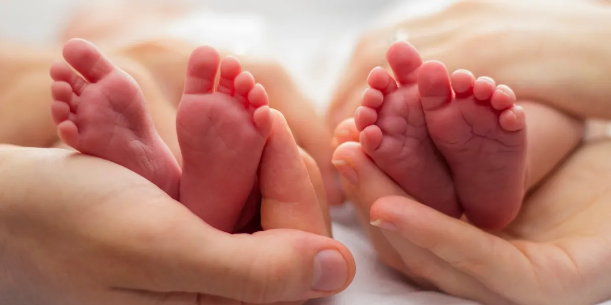 mother and father's hands cradling twin babies' feet on a pale background