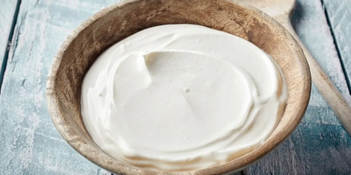 bowl of thick creamy natural greek yogurt on a rustic wood table with a wooden spoon alongside
