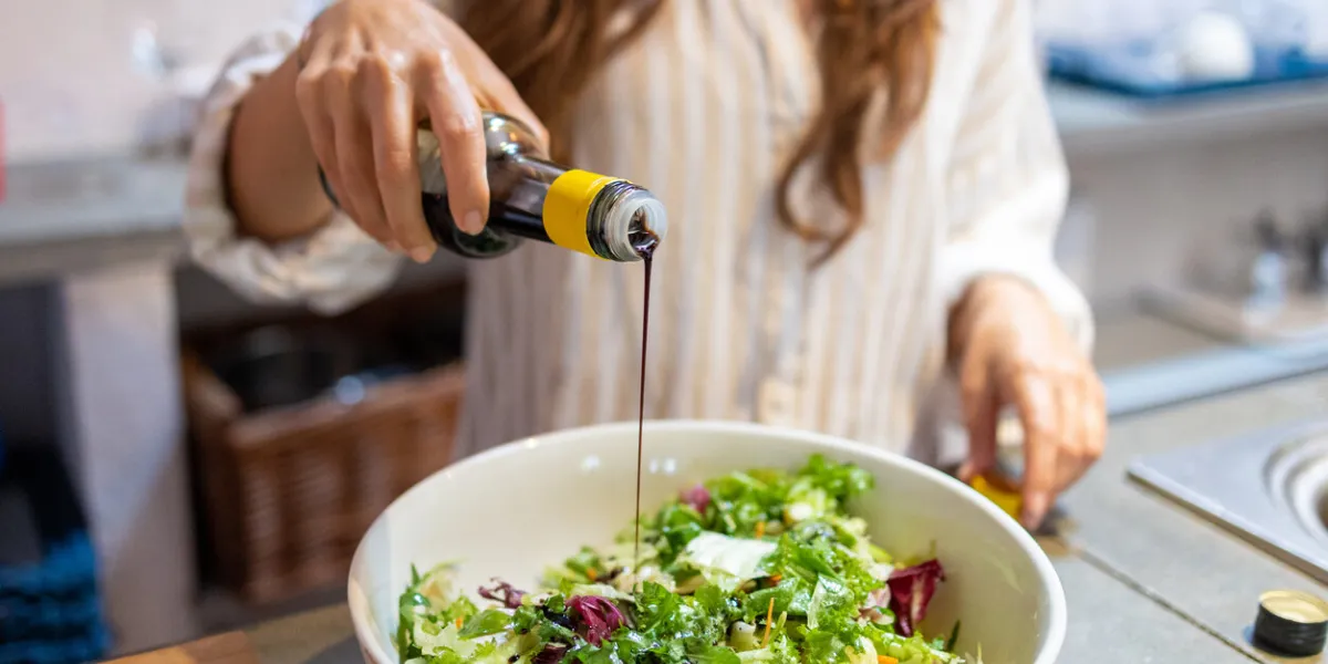 female hand pouring balsamic vinegar on the fresh vegetables salad