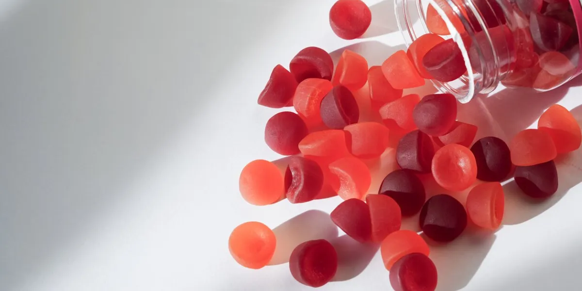 a transparent bottle spills red and orange gummy vitamins onto a clean, white surface