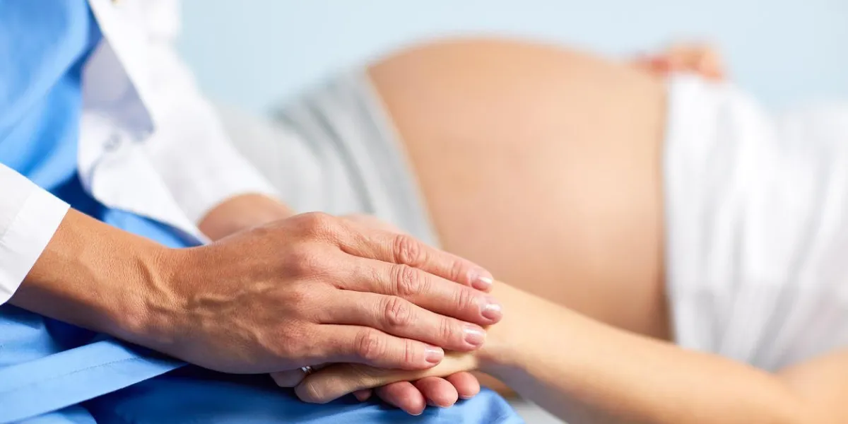 main de l'assistant ou de l'infirmière tenant celle d'une femme enceinte