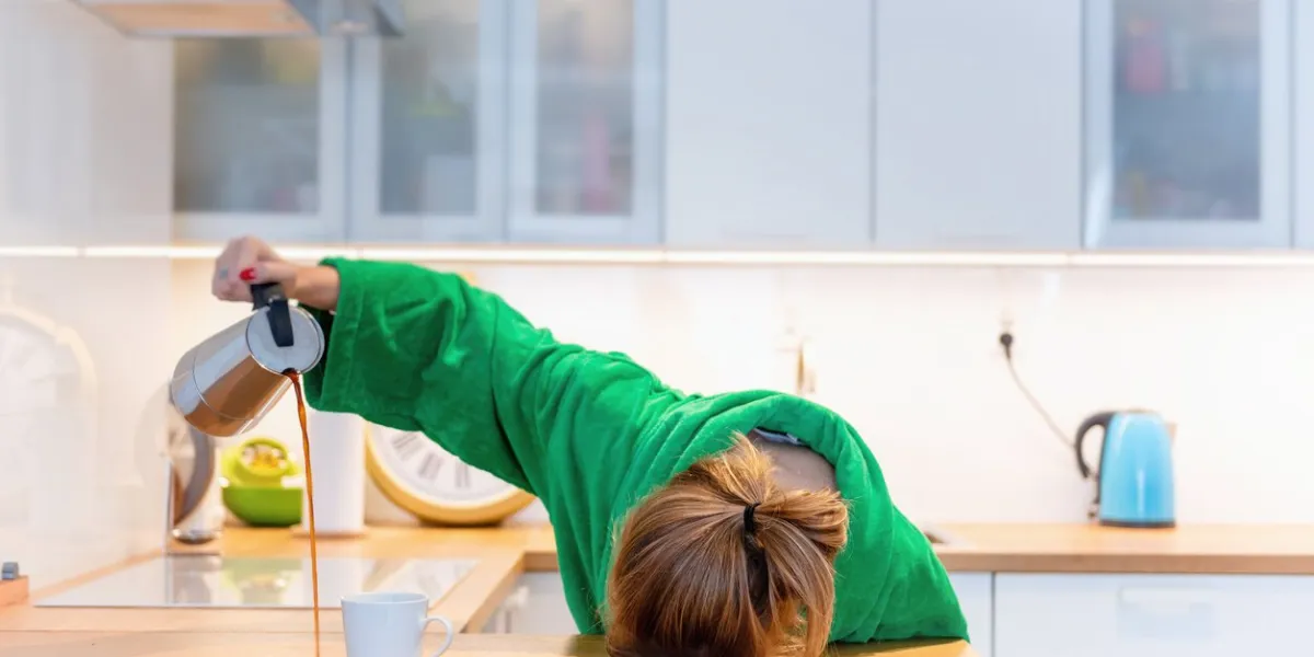 tired woman sleeping on the table in the kitchen at breakfast trying to drink morning coffee