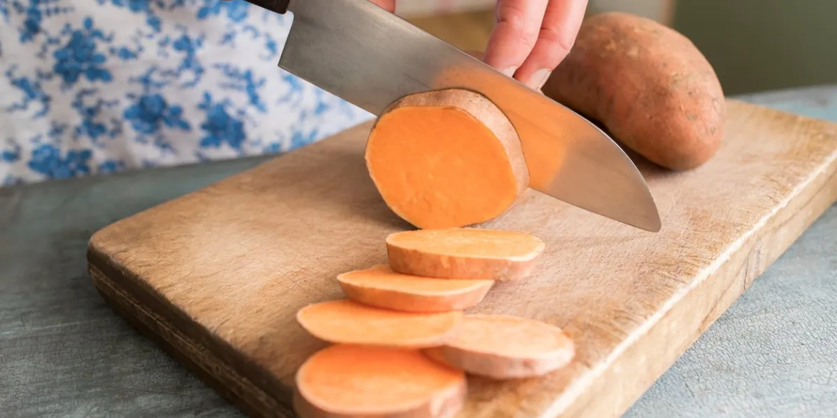 close up of woman preparing sweet potato on chopping board